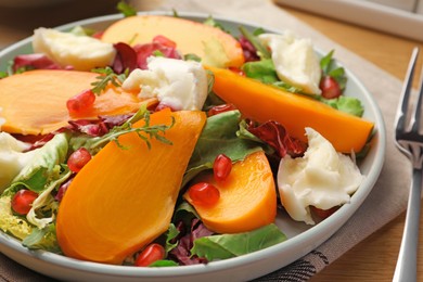 Photo of Delicious persimmon salad with cheese and pomegranate served on wooden table, closeup