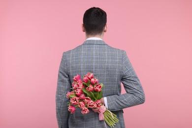 Man hiding beautiful bouquet on pink background, back view