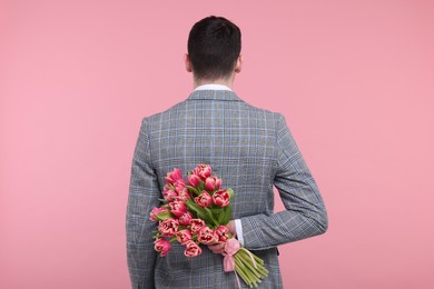 Photo of Man hiding beautiful bouquet on pink background, back view