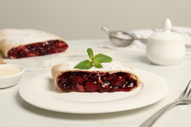 Photo of Delicious strudel with cherries, powdered sugar and mint on white table