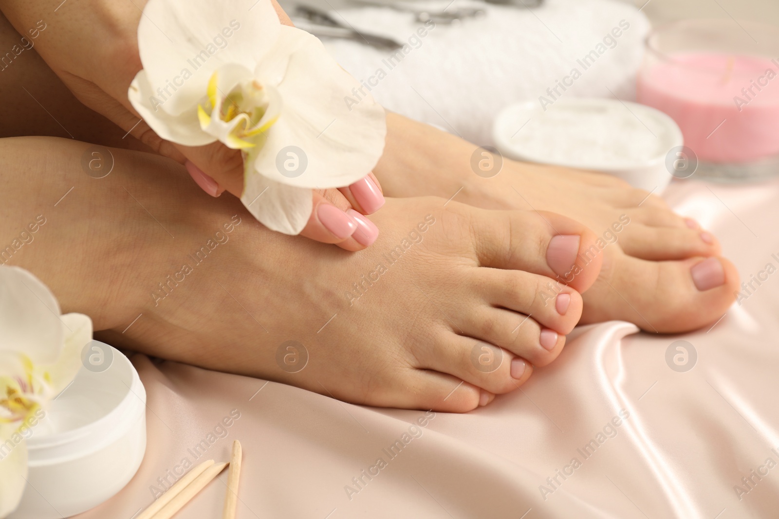 Photo of Woman with neat toenails after pedicure procedure on silk fabric, closeup