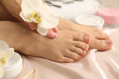 Woman with neat toenails after pedicure procedure on silk fabric, closeup