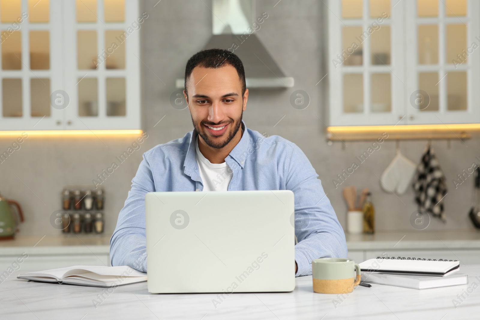 Photo of Young man working on laptop at desk in kitchen. Home office