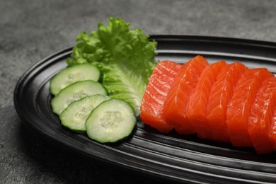 Photo of Tasty salmon slices, cucumber and lettuce on grey table, closeup. Delicious sashimi dish