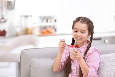 Cute girl eating tasty yogurt at home