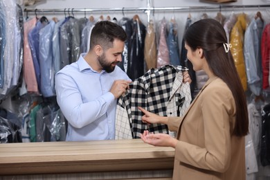 Photo of Dry-cleaning service. Happy worker receiving shirt from client indoors