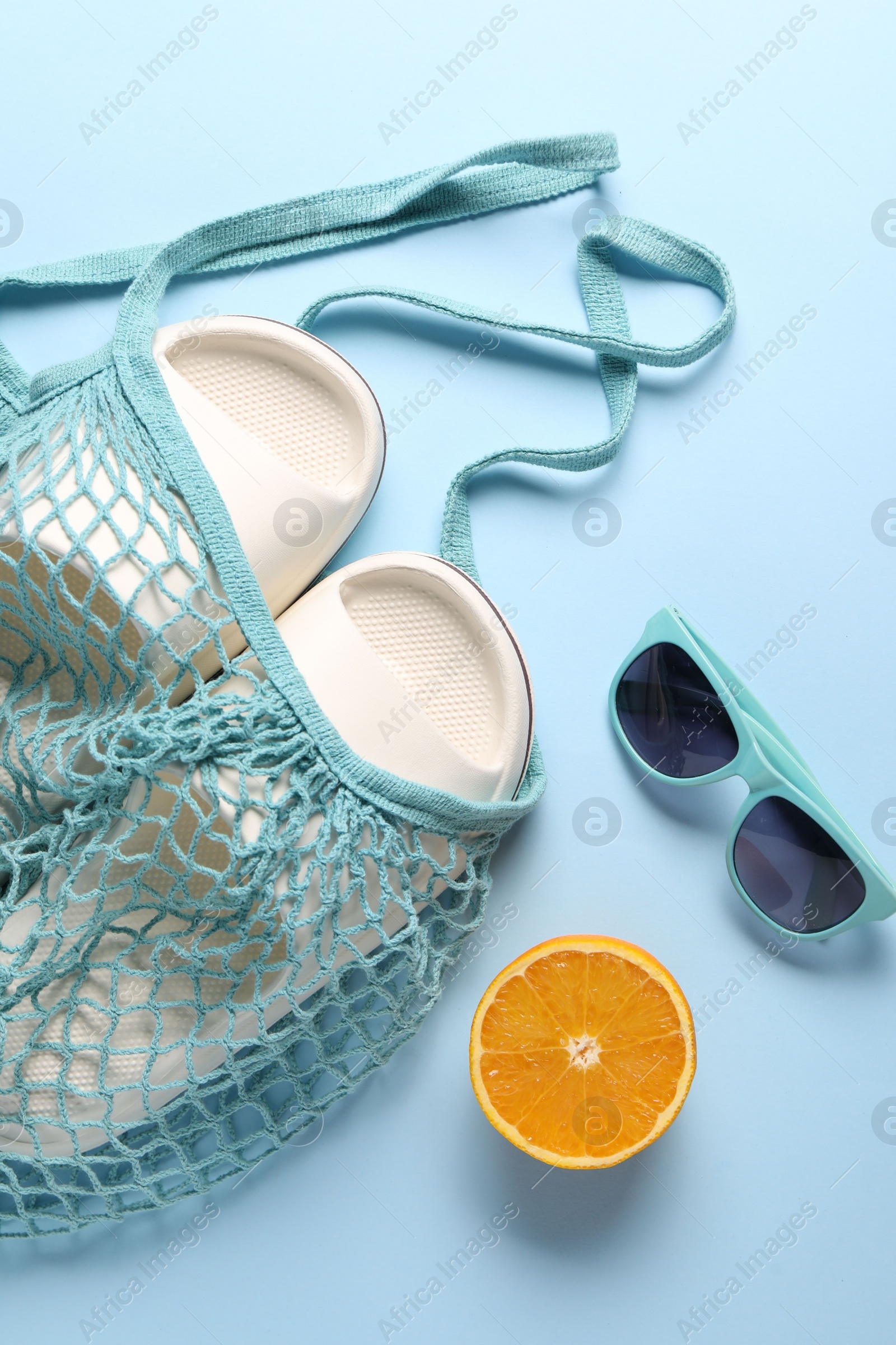 Photo of String bag, sunglasses, orange and slippers on light blue background, top view