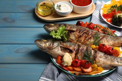 Photo of Plate with delicious baked sea bass fish and vegetables on light blue table