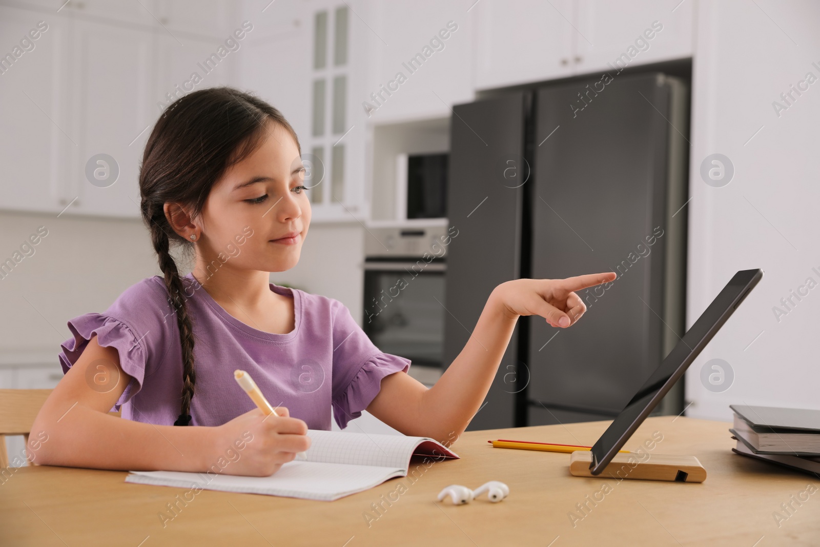 Photo of Little girl doing homework with modern tablet at home