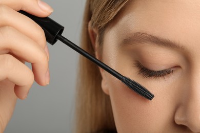 Woman applying mascara onto eyelashes against grey background, closeup