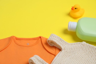 Photo of Bottles of laundry detergents, baby clothes and rubber duck on yellow background. Space for text