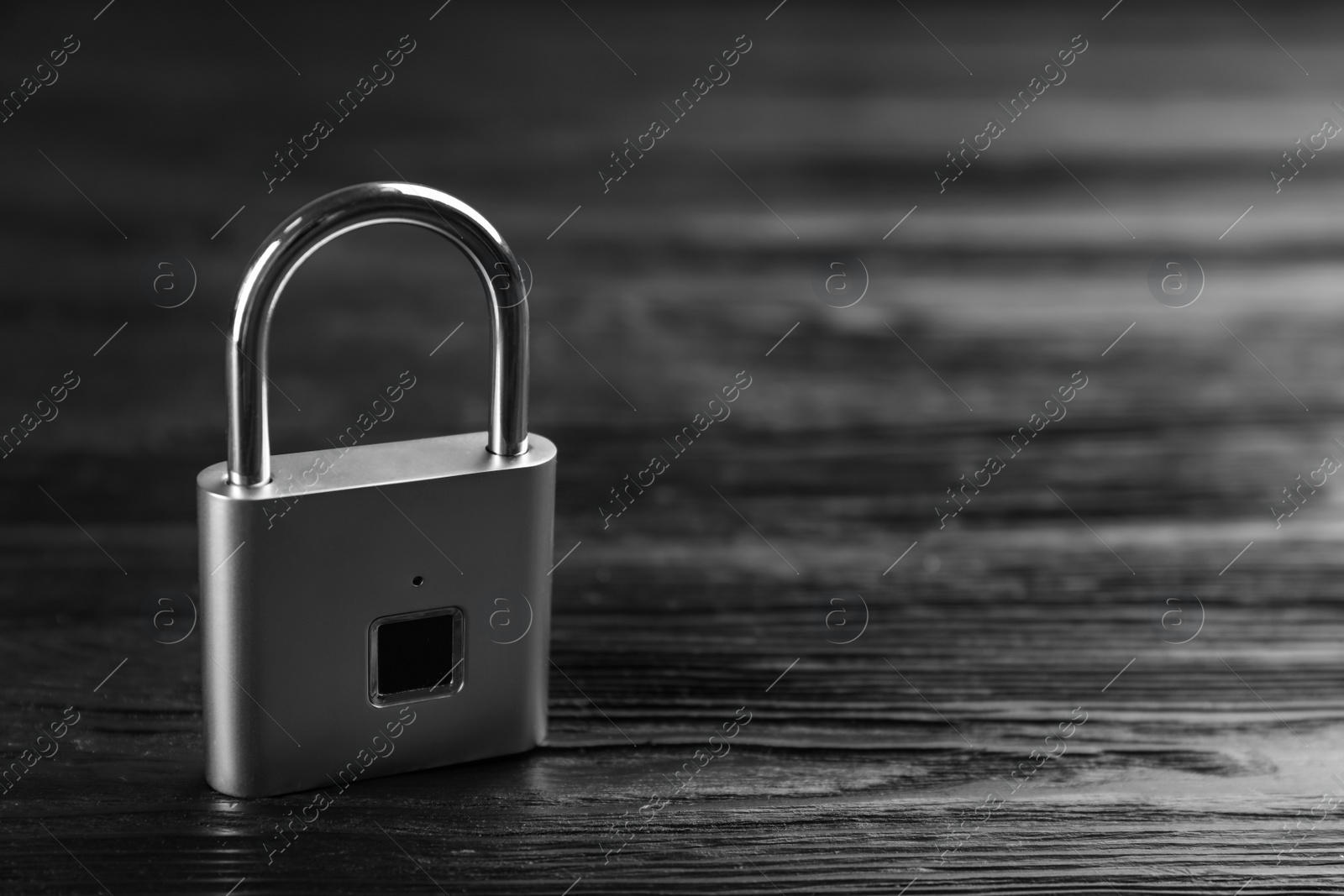 Photo of Modern padlock on black wooden table. Space for text
