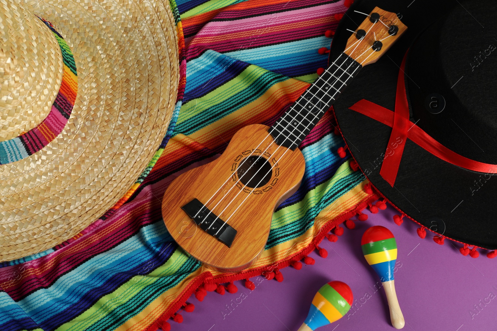 Photo of Flat lay composition with Mexican sombrero and black Flamenco hats, ukulele and maracas on purple table