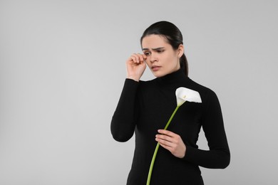 Photo of Sad woman with calla lily flower mourning on light grey background, space for text. Funeral ceremony