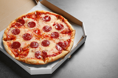 Photo of Hot delicious pepperoni pizza in cardboard box on grey table