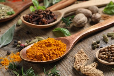 Different herbs and spices with spoons on wooden table, closeup