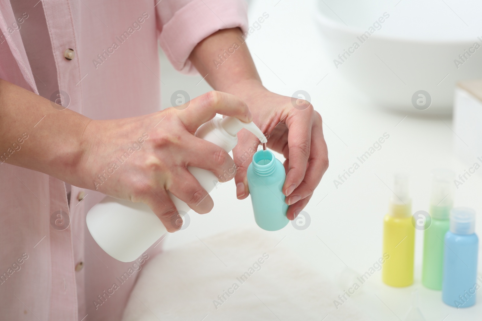 Photo of Woman pouring cosmetic product into plastic bottle over white countertop indoors, closeup and space for text. Bath accessories