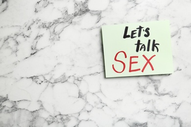 Photo of Note with phrase "LET'S TALK SEX" on marble background, top view. Space for text