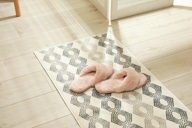 Photo of New stylish bath mat with fluffy slippers on floor indoors