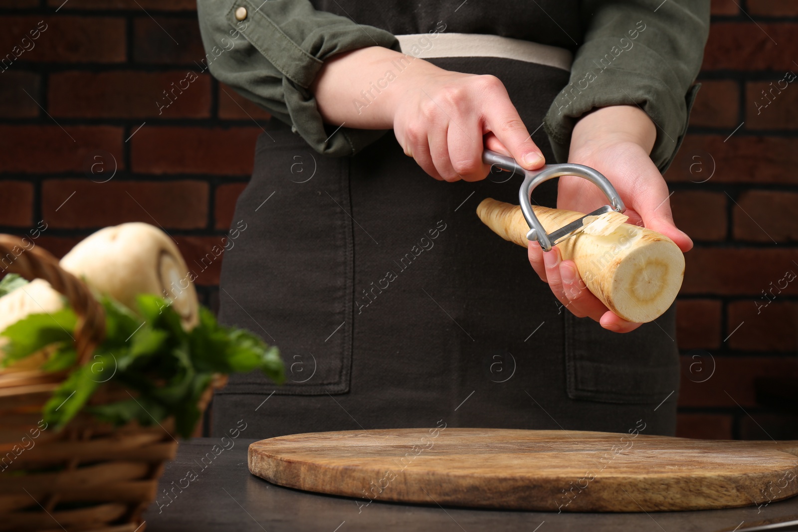 Photo of Woman peeling fresh ripe parsnip at black table, closeup