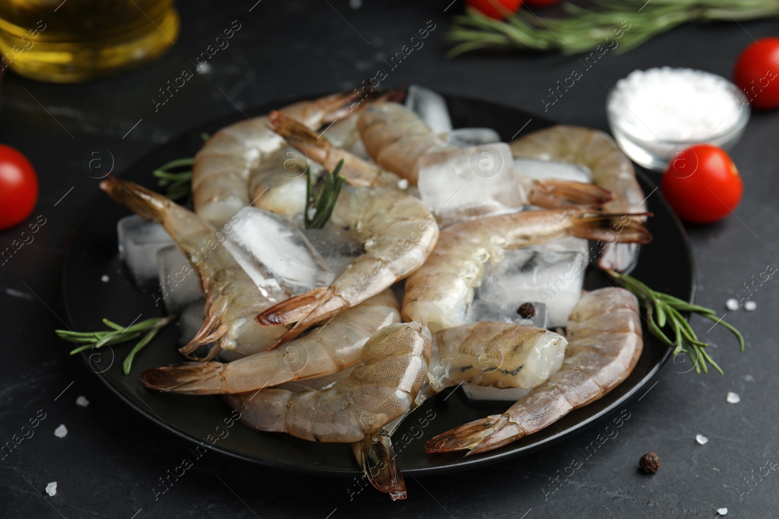 Photo of Fresh raw shrimps with rosemary and ice cubes on black table