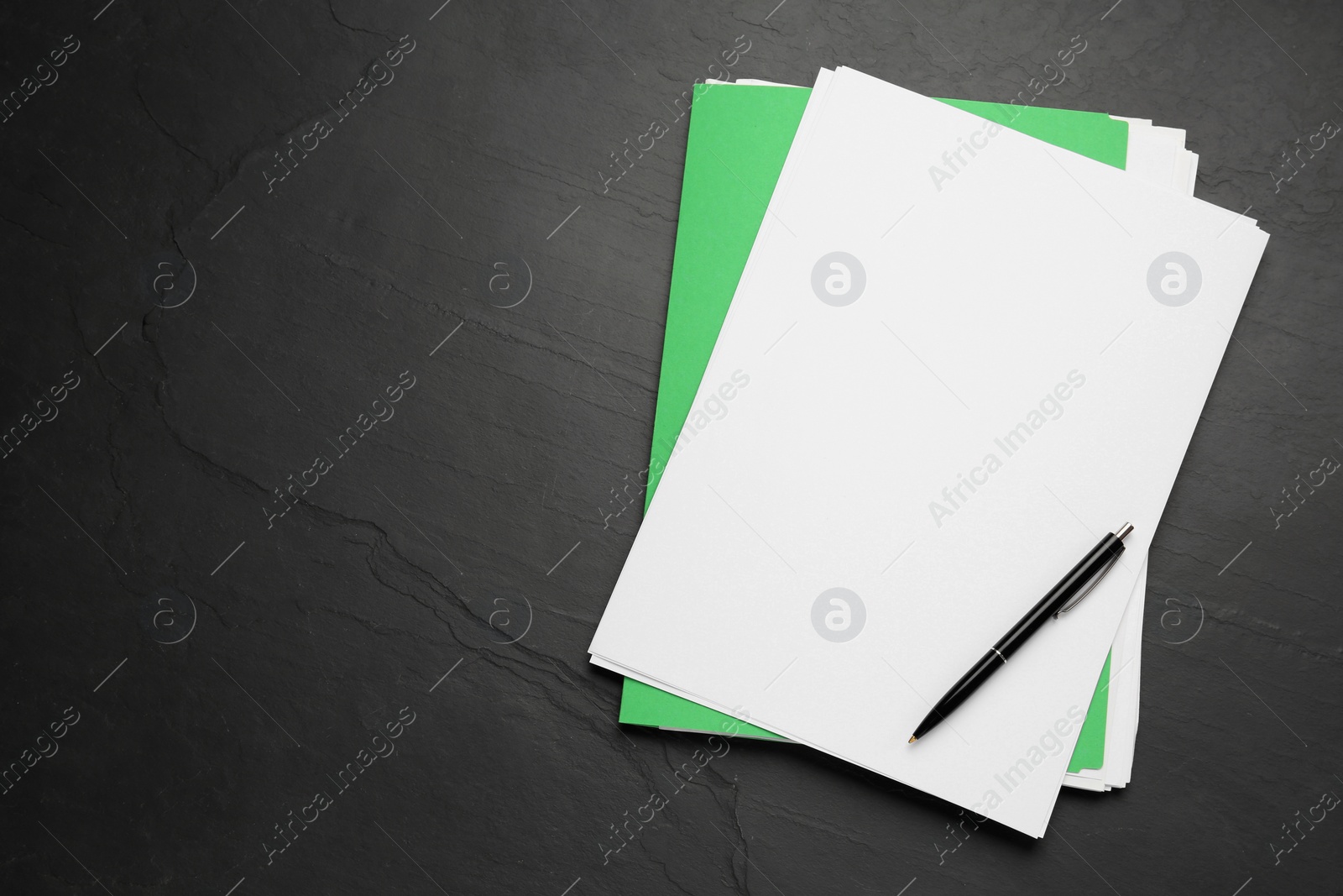 Photo of Light green file with blank sheets of paper and pen on black slate table, top view. Space for text