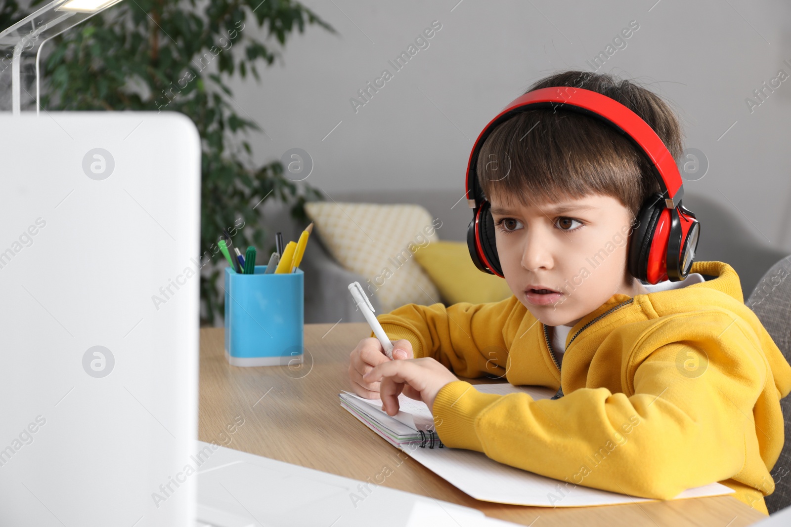 Photo of Cute little boy with modern laptop studying online at home. E-learning