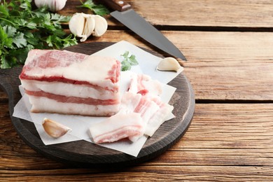Photo of Tasty salt pork with garlic and parsley on wooden table, space for text