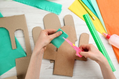 Photo of Woman cutting green paper at white wooden table, top view. Pinata DIY