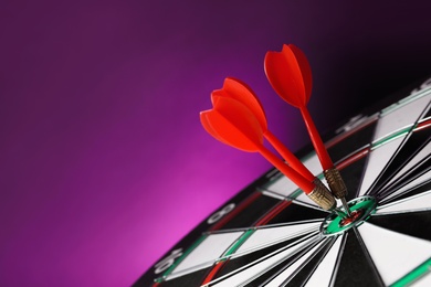 Photo of Red arrows hitting target on dart board against purple background. Space for text