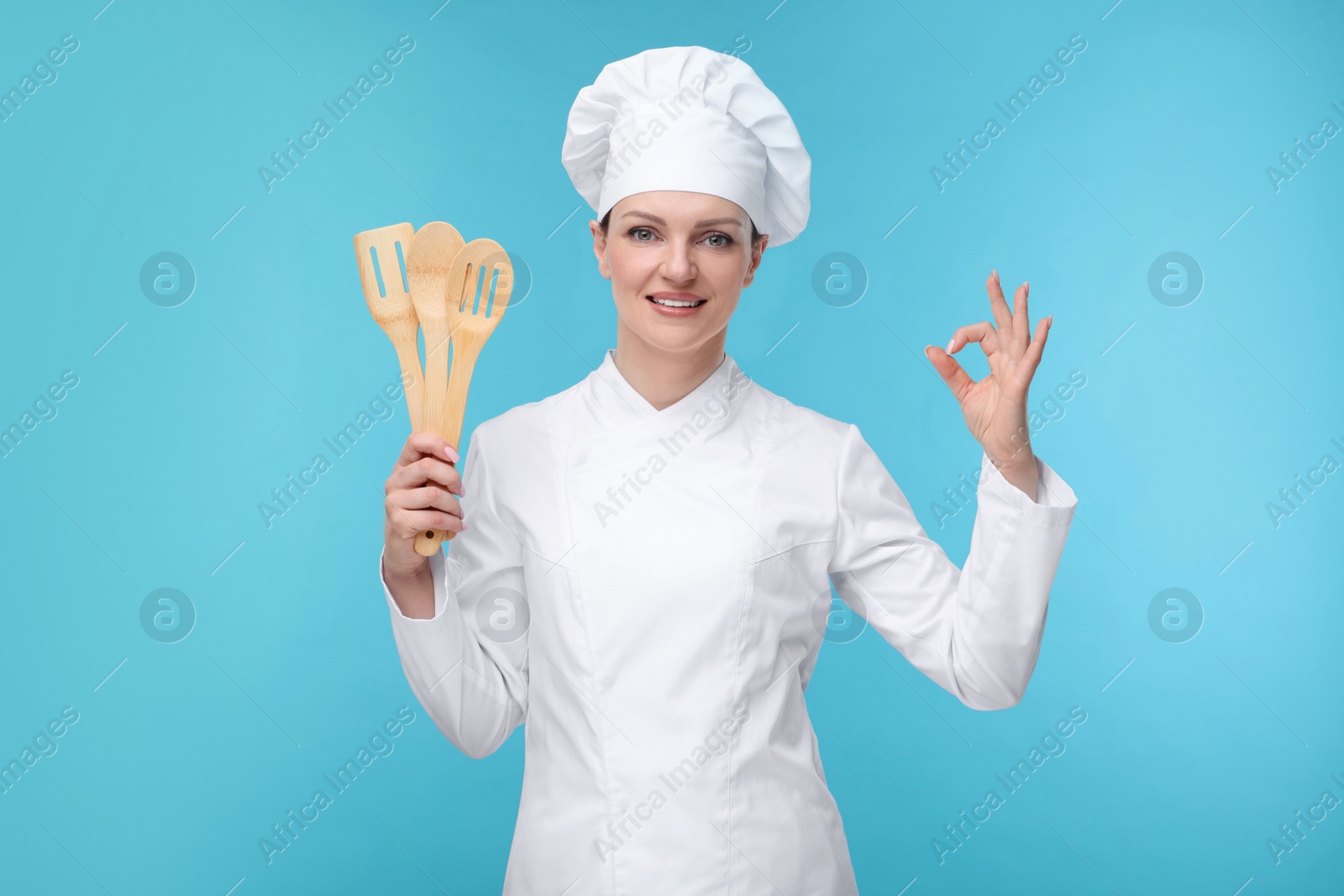 Photo of Happy chef in uniform holding wooden utensils on light blue background