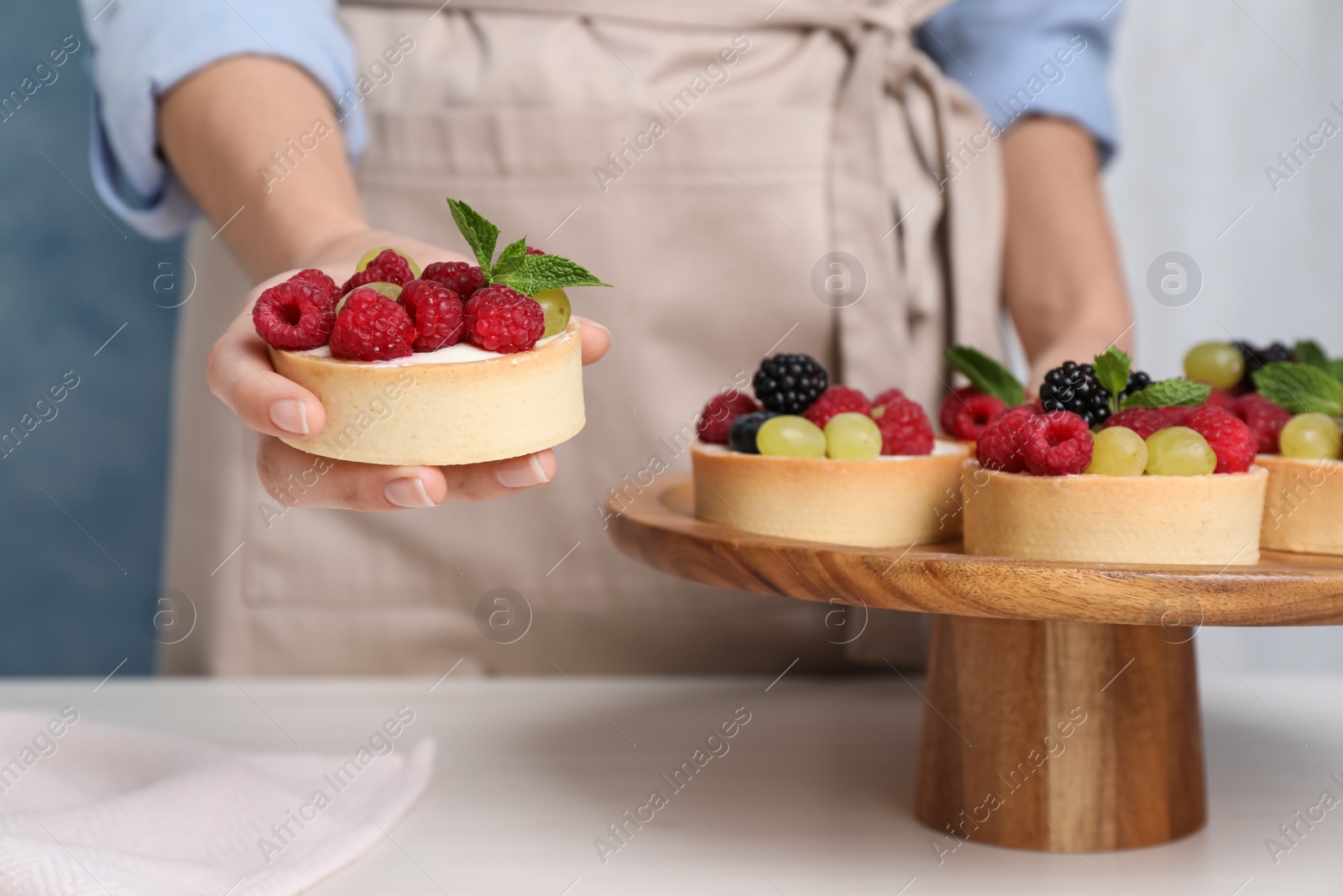 Photo of Woman with delicious tartlets at white table, closeup