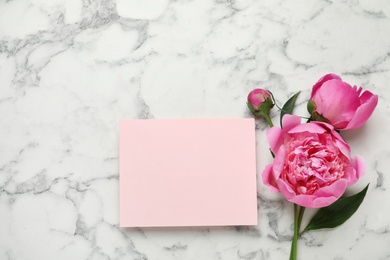 Fragrant peonies and blank card on marble table, top view with space for text. Beautiful spring flowers