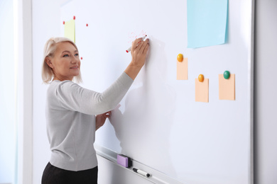 Photo of Mature teacher writing on whiteboard in classroom