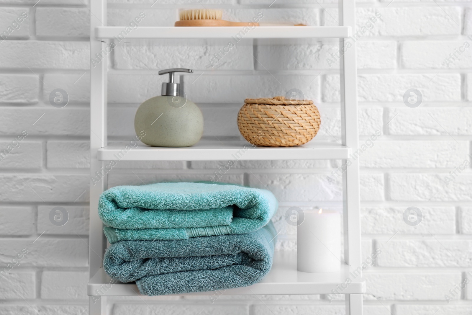 Photo of Clean soft towels and soap dispenser on shelves near white brick wall