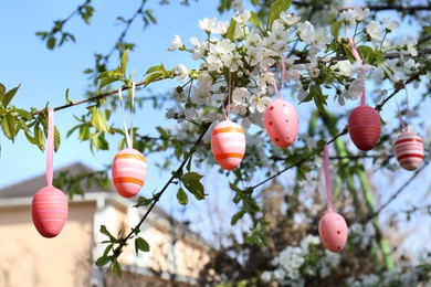 Photo of Beautifully painted Easter eggs hanging on blooming tree outdoors