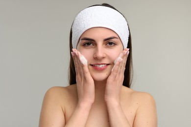 Photo of Young woman with headband washing her face on light grey background