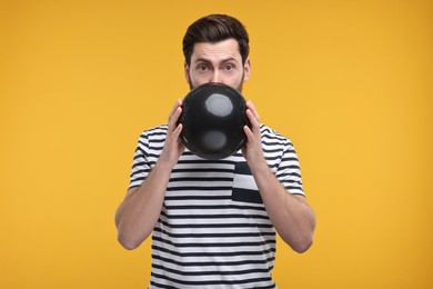 Photo of Man inflating black balloon on yellow background