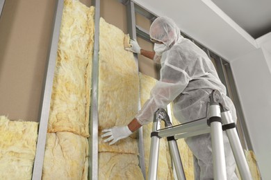Photo of Worker insulating wall using ladder indoors, low angle view