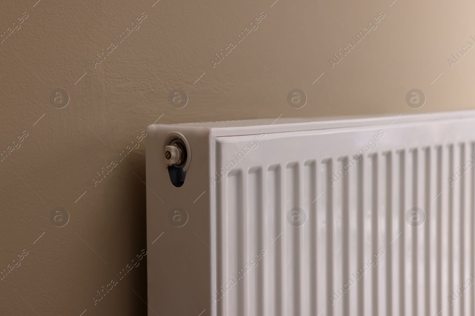 Photo of Modern radiator on beige wall, closeup. Central heating system