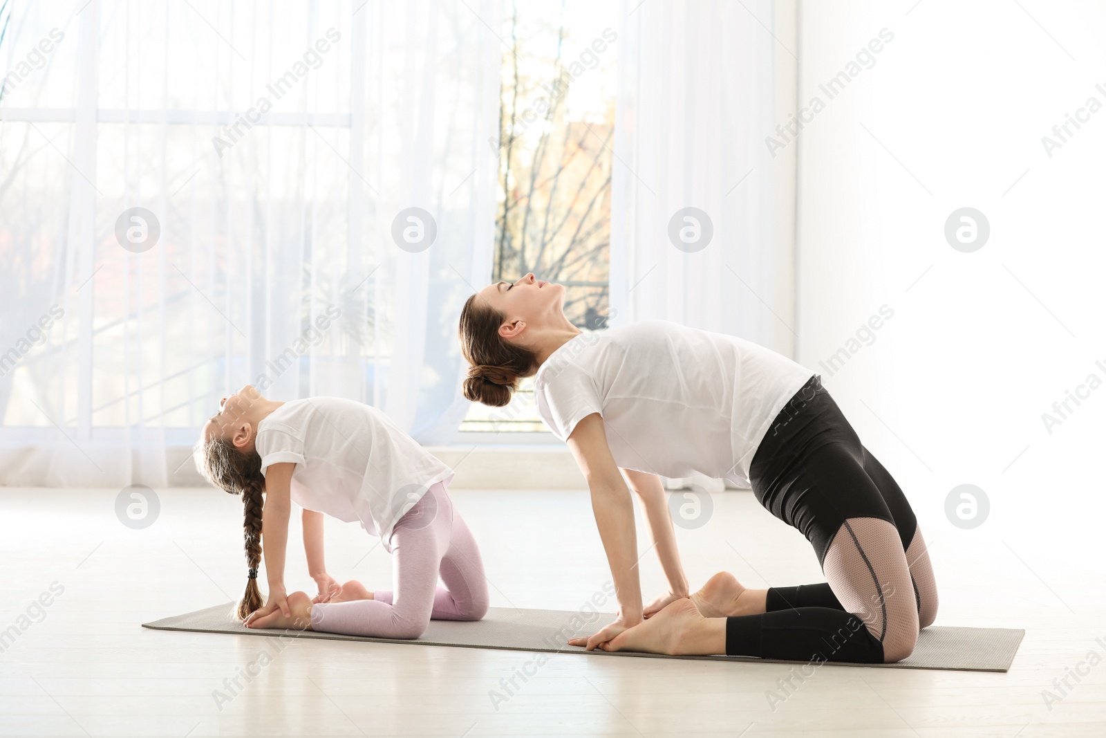 Photo of Young mother with little daughter practicing yoga at home