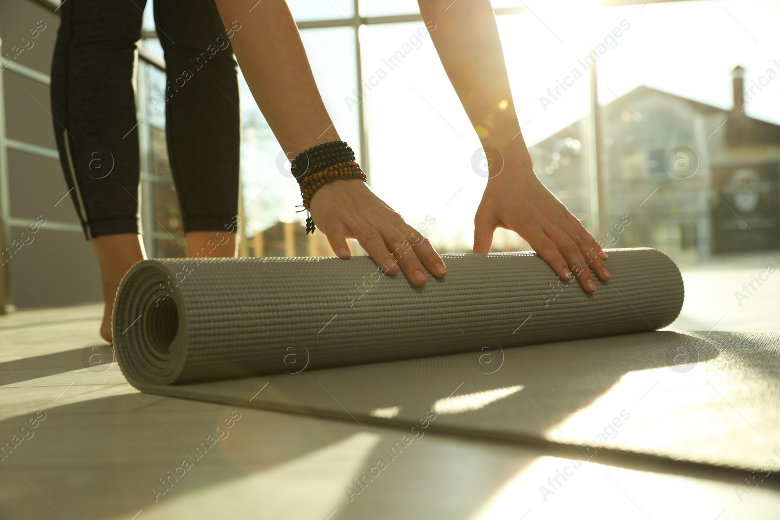 Photo of Young woman rolling yoga mat in sunlit room, closeup