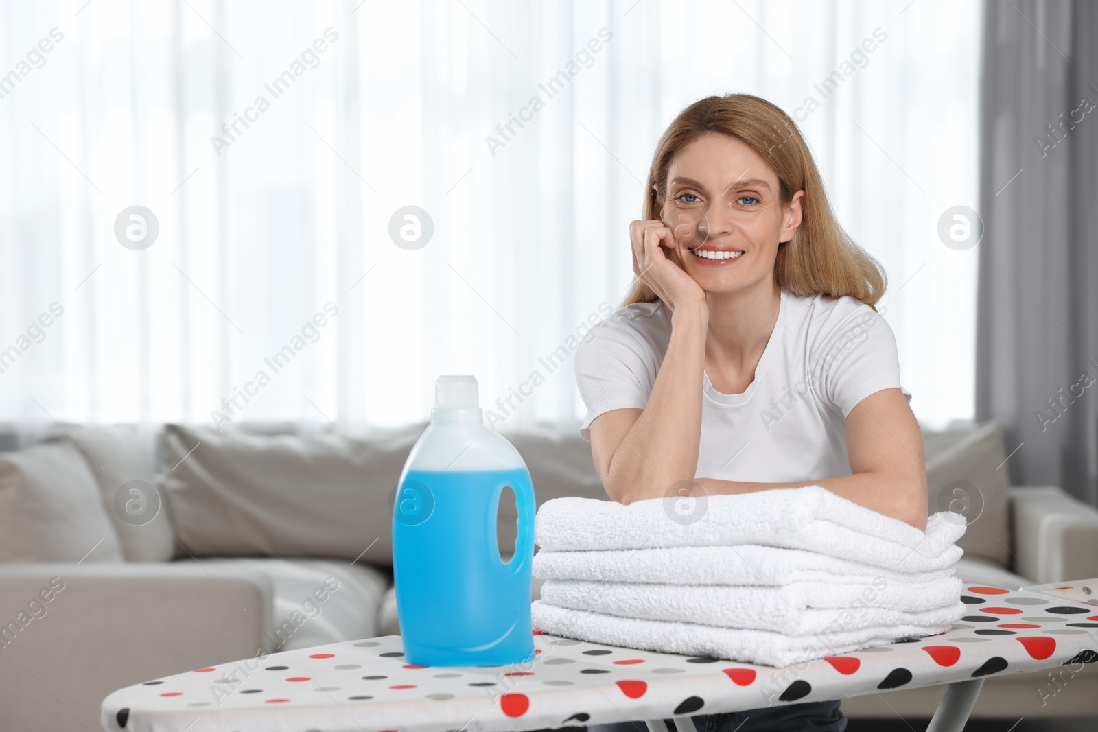 Photo of Woman with fabric softener and clean towels in room, space for text