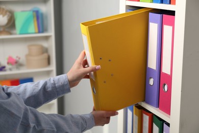 Woman taking binder office folder from shelving unit indoors, closeup