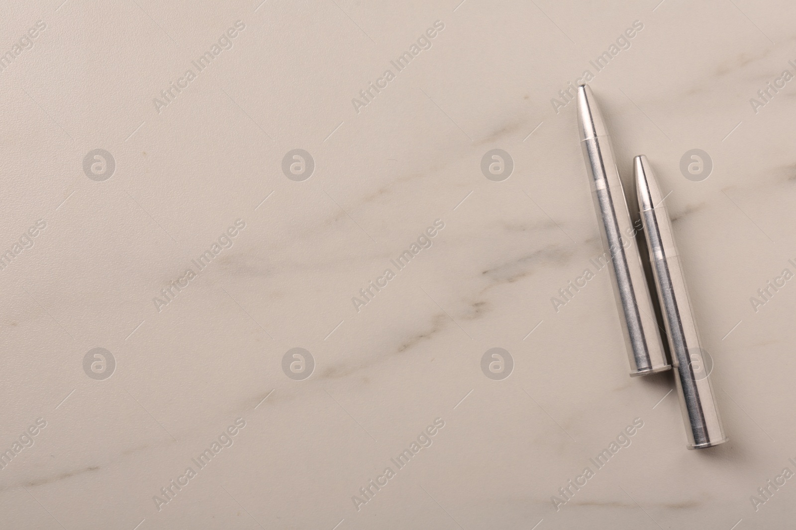 Photo of Two metal bullets on light marble table, flat lay. Space for text