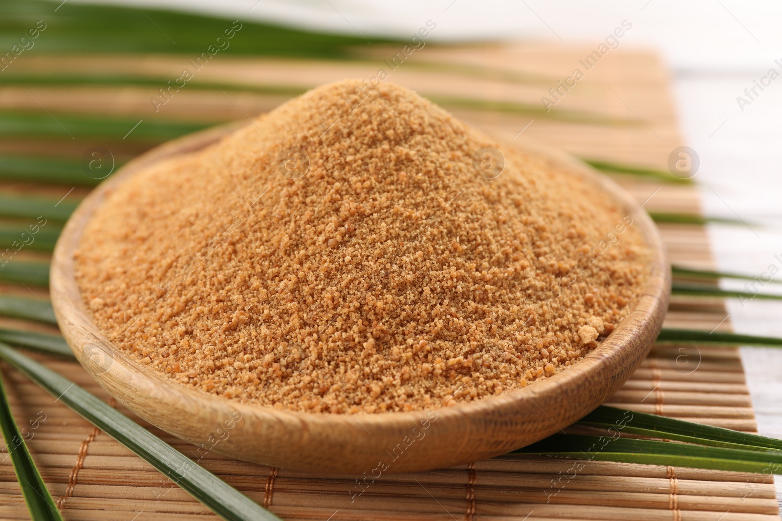 Photo of Coconut sugar, palm leaves and bamboo mat on table, closeup