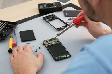 Technician repairing broken smartphone at table, closeup