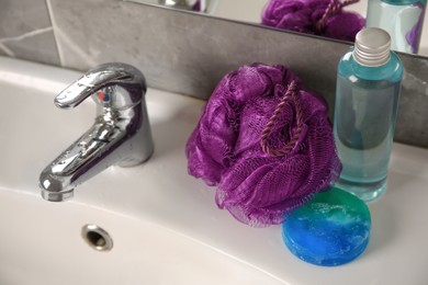 Photo of Purple shower puff and cosmetic products on sink in bathroom