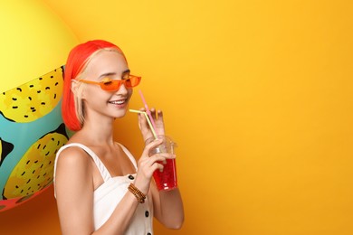 Photo of Beautiful young woman with bright dyed hair holding refreshing cocktail near inflatable ball on orange background, space for text