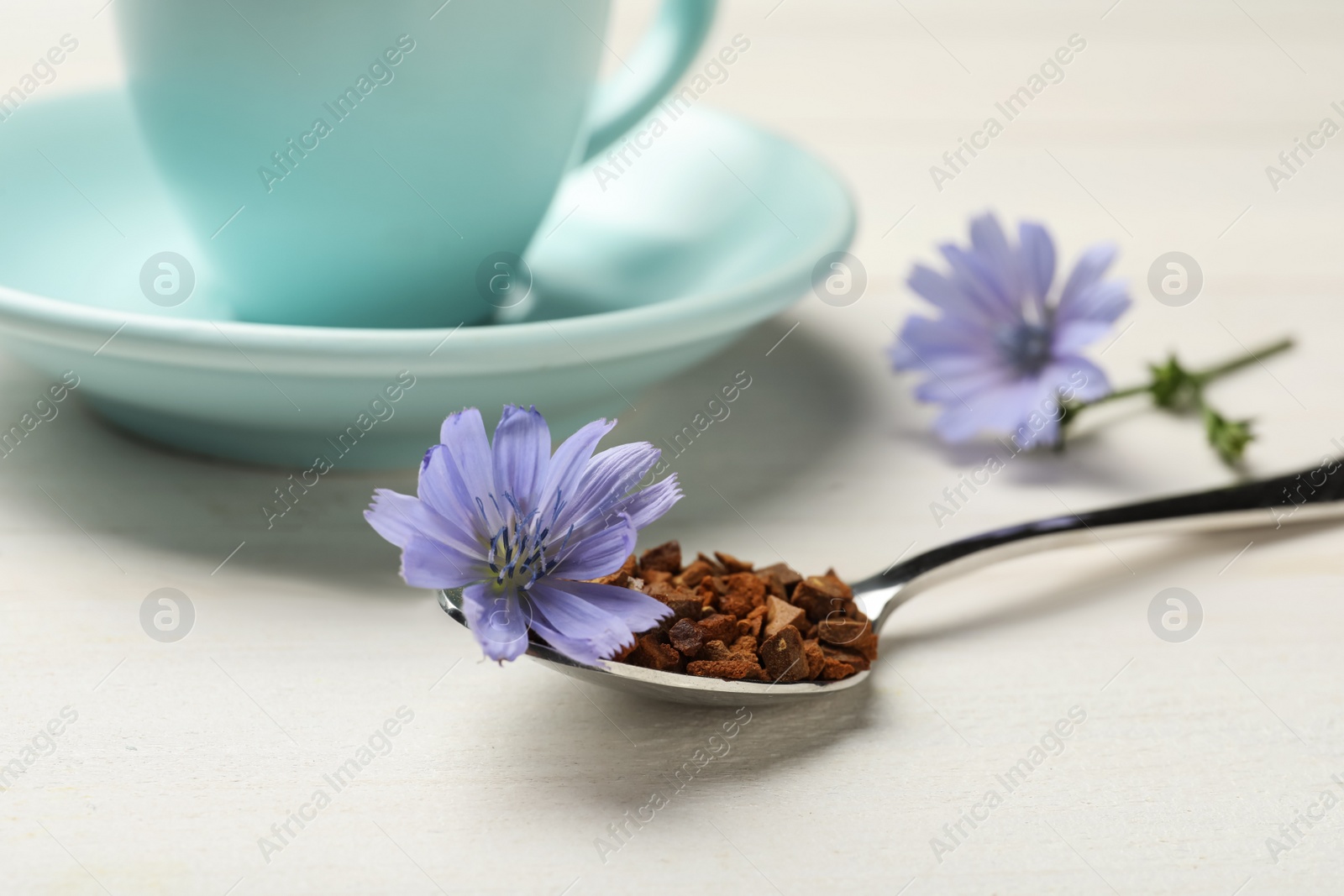Photo of Spoon of chicory granules with flower on white wooden table, closeup